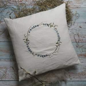 May include: A white pillow with a floral embroidery design. The embroidery is a wreath of blue and white flowers.