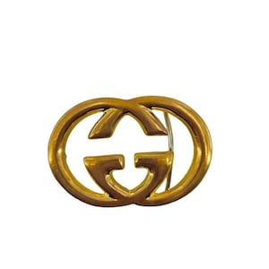 May include: A gold-toned metal pin featuring the interlocking double G logo, a signature design element of the Italian luxury brand Gucci.