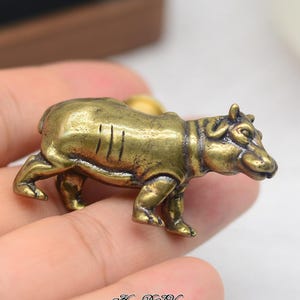 May include: A miniature brass hippopotamus figurine. The sculpture, in a walking stance, shows intricate detailing and lines. The golden-brown figurine is likely a decorative piece, with a vintage aesthetic.