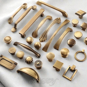 Può includere: Una collezione di ferramenta per mobili in ottone antico, tra cui pomelli, maniglie e tiranti. L'hardware presenta vari design, dai semplici pomelli rotondi ai tiranti curvi e ornati. I pezzi sono disposti su una superficie bianca.