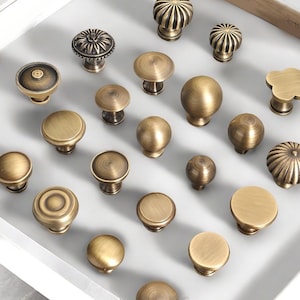 May include: A collection of antique brass cabinet knobs in various designs. The knobs include round, fluted, and floral styles, all with a warm, aged finish. These decorative hardware pieces are ideal for furniture restoration or adding vintage charm.