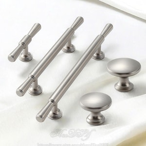 May include: A set of brushed nickel cabinet hardware, including two long bar pulls, a shorter bar pull, and two round knobs. The hardware has a modern design with a matte finish, suitable for drawers and cabinets.