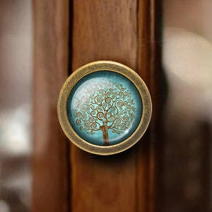 May include: A round, antique brass cabinet knob with a glass insert featuring a blue and gold tree of life design.