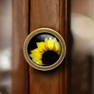 Może przedstawiać: Okrągły, antyczny, złoty gałka do szafki z wkładką szklaną przedstawiającą zbliżenie żółtego słonecznika.