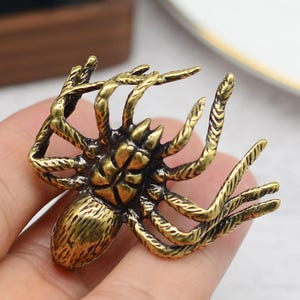 Może przedstawiać: Szczegółowa figurka pająka w kolorze brązu z ośmioma nogami i teksturowanym korpusem. Pająk jest w pozycji pełzającej, z rozłożonymi nogami. Nazwa i adres URL sklepu Etsy są widoczne na dole obrazu.