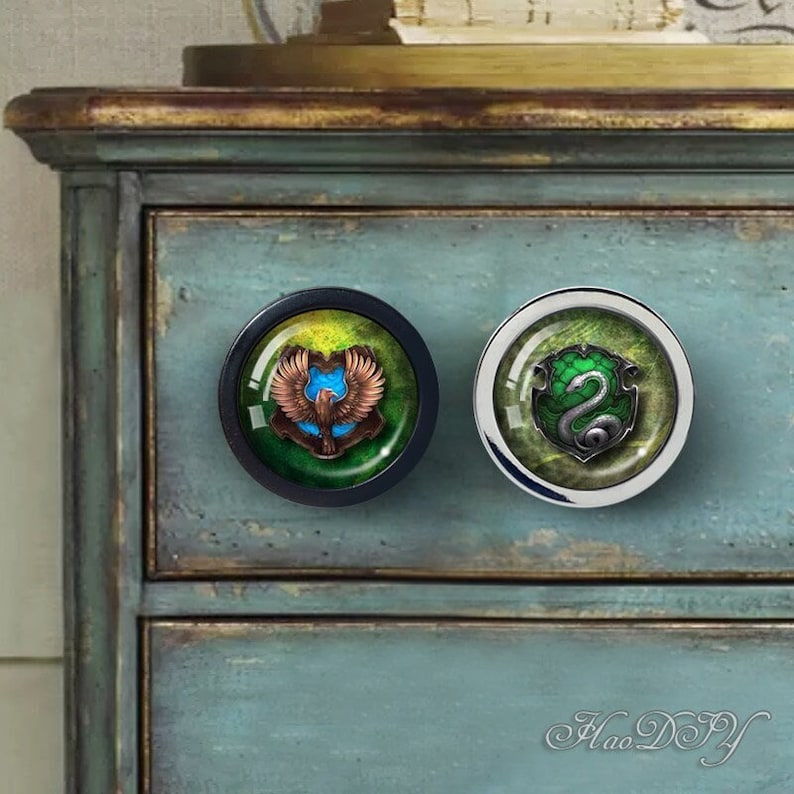 May include: Two round cabinet knobs with a green, gold, and blue design. The left knob features a golden eagle with outstretched wings and the right knob features a green snake with a silver shield.
