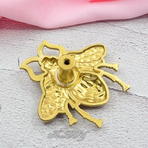 Peut inclure: Un bouton de meuble dor&eacute; en forme d'abeille. Le bouton pr&eacute;sente des motifs d&eacute;taill&eacute;s d'ailes et de corps, avec une vis centrale pour le montage. La conception comprend des antennes et des pattes, ajoutant &agrave; l'apparence r&eacute;aliste de l'abeille. Le texte "Hao-DIY" est en bas.