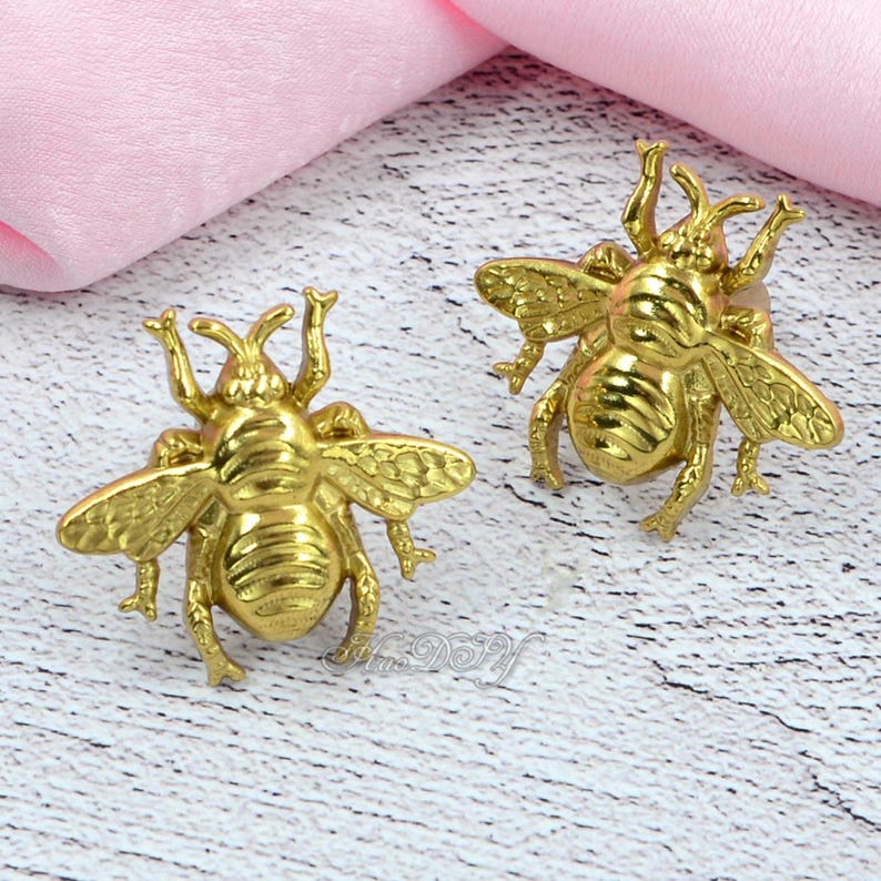May include: Two gold-coloured bee-shaped decorative objects. The bees have detailed wings, antennae, and body segments. These are likely decorative accents or embellishments.
