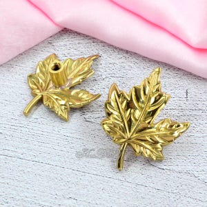 May include: Two gold-colored leaf-shaped cabinet knobs. The knobs have detailed veining and a threaded post for attachment. The leaves are a bright, shiny gold color. The knobs are likely made of metal and are suitable for furniture or decorative projects.