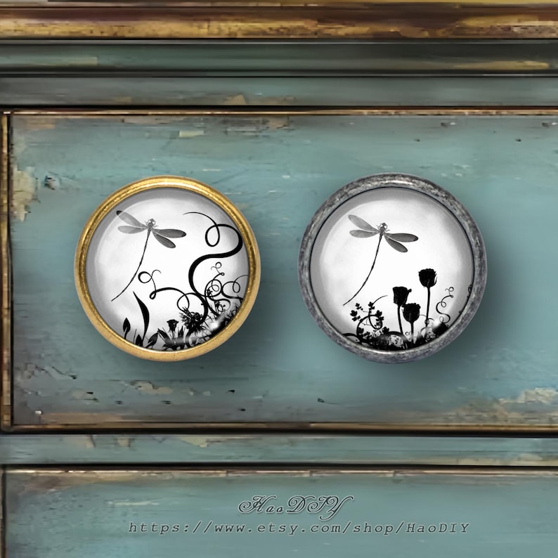 May include: Two round cabinet knobs with dragonfly designs. One knob has a gold-colored frame, the other a silver-colored frame. The dragonfly and floral designs are in black and white, set against a white background.