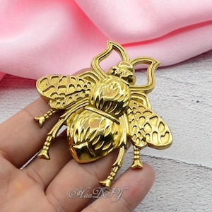 May include: A gold-colored bee-shaped decorative element. The bee has detailed wings, legs, and body segments. The image shows the bee against a pink background. The text "Hao DIY" is visible at the bottom.