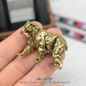 Könnte beinhalten: Detaillierte Bärenfigur aus Messing im antiken Stil. Der Bär wird in einer Laufpose dargestellt, mit strukturiertem Fell und einem detaillierten Gesicht. Die Figur hat eine Vintage-Ästhetik mit einem warmen, goldenen Farbton. Der Etsy-Shop-Name und die URL sind unten sichtbar.