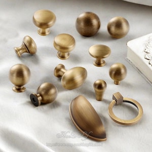 May include: A collection of antique brass cabinet knobs and pulls in various shapes and sizes. The hardware includes round, oval, and ring-shaped designs, all with a warm, aged finish. Ideal for furniture restoration or adding vintage charm.
