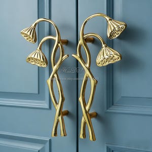 May include: Two gold door handles with a floral design. The handles are shaped like curved stems with lotus flower-shaped ends. The handles are mounted on a blue door.