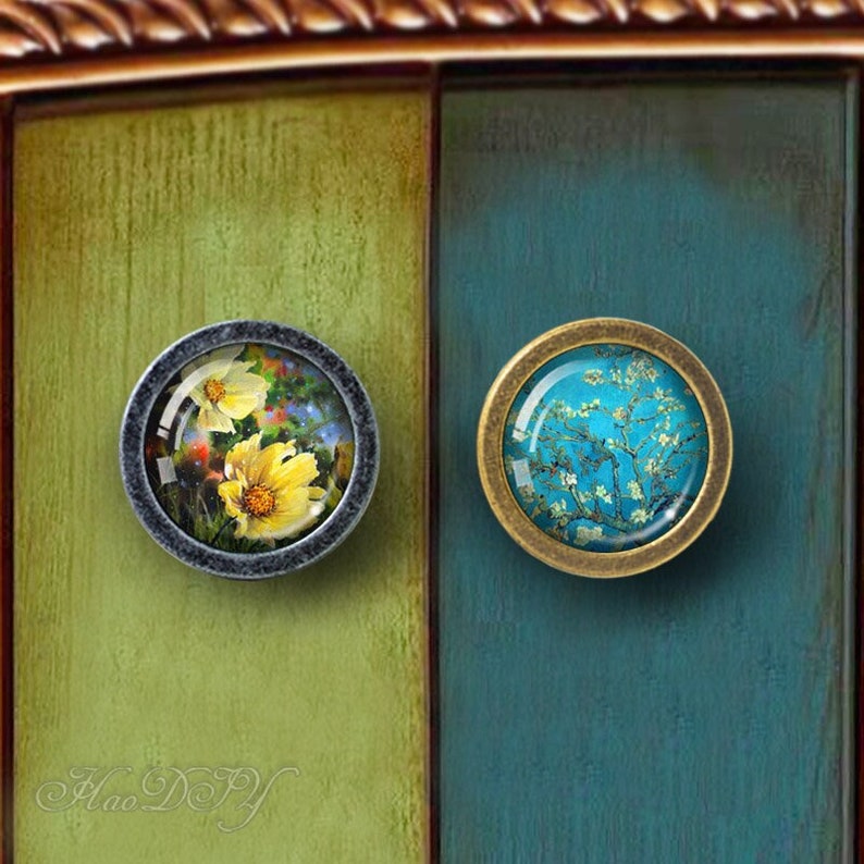 Peut inclure: Deux boutons ronds pour armoire avec des motifs floraux. Le bouton de gauche a une base en m&eacute;tal gris et un insert en verre avec un motif de fleur jaune. Le bouton de droite a une base en laiton et un insert en verre avec un motif floral bleu et blanc.