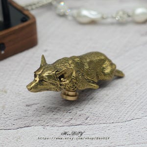 May include: A brass corgi-shaped wax seal stamp. The stamp is detailed with the corgi's features and is mounted on a brass base. The Etsy shop URL is visible at the bottom of the image.