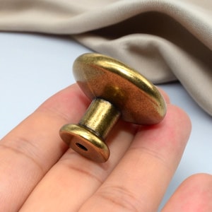 Puede incluir: Pomo de armario de lat&oacute;n antiguo con una parte superior redondeada y una base cil&iacute;ndrica. El pomo tiene una est&eacute;tica vintage, adecuado para la restauraci&oacute;n de muebles o para a&ntilde;adir un toque cl&aacute;sico a armarios y cajones.