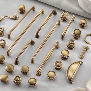 Op de afbeelding: Een verzameling antieke messing kastbeslagen, waaronder knoppen, grepen en handgrepen. De hardware heeft verschillende ontwerpen, van eenvoudige ronde knoppen tot sierlijke grepen met decoratieve details.