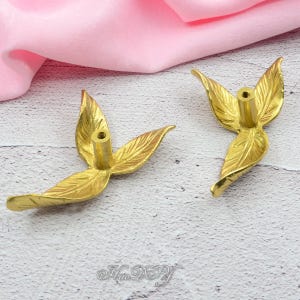 Pu&ograve; includere: Due pomelli dorati a forma di foglia. Ogni pomello presenta un perno filettato centrale per il montaggio e due foglie stilizzate con venature dettagliate. I pomelli sono in metallo e hanno una finitura lucida. Lo sfondo &egrave; un tessuto rosa.