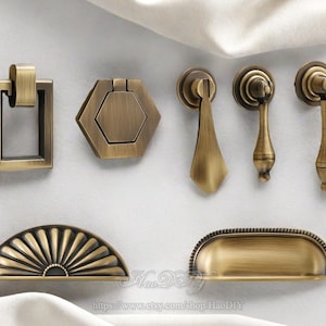 Könnte beinhalten: Eine Auswahl an antiken Messing-Schrankgriffen und -Zügen. Die Kollektion umfasst einen rechteckigen Griff, einen sechseckigen Griff, drei Tropfengriffe und einen halbmondförmigen Griff mit Fächerdesign. Auf neutralem Hintergrund.