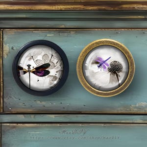 Puede incluir: Dos pomos redondos para armarios con dise&ntilde;os de lib&eacute;lulas. Uno tiene un marco negro y presenta una lib&eacute;lula con acentos morados y verdes sobre un fondo blanco y gris. El otro pomo tiene un marco dorado y una lib&eacute;lula morada.