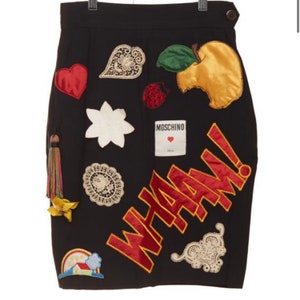 May include: Black skirt with various colorful embroidered patches, including a red heart, a white flower, a green apple, a ladybug, a lace design, and the word "WHAM!" in red and yellow.