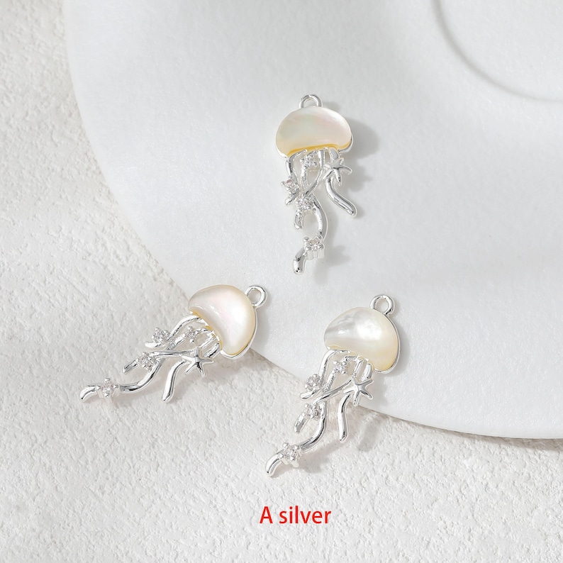 May include: Three silver-colored jellyfish charms with pearlescent tops and dangling tendrils. The charms have a loop at the top for attaching to jewelry. The text "A silver" is at the bottom of the image.