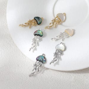 May include: Six jellyfish-shaped pendants with iridescent shells and intricate metalwork. The pendants are in gold and silver tones, with some featuring clear gemstone accents. The shells have a pearlescent sheen, adding to their delicate appearance.