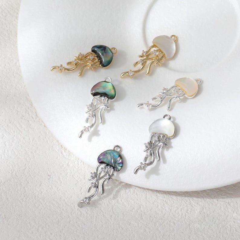 May include: Six jellyfish-shaped pendants with iridescent shells and intricate metalwork. The pendants are in gold and silver tones, with some featuring clear gemstone accents. The shells have a pearlescent sheen, adding to their delicate appearance.