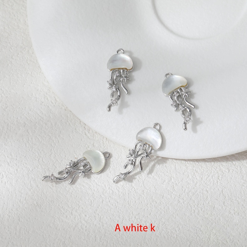 May include: Four silver-toned jellyfish charms with white shell-like caps and intricate tentacle details. Each charm has a small loop for attaching to jewelry. The text "A white k" is at the bottom.
