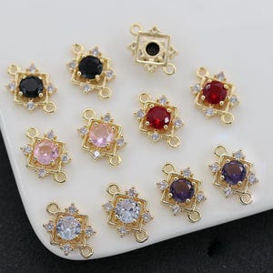 May include: Ten gold-tone connector charms with different coloured rhinestones. Each charm features a square design with a central rhinestone and smaller rhinestones around the edge.