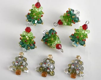 May include: A collection of handmade Christmas tree ornaments. The ornaments are made of green, red, and clear beads, with gold accents. Some trees have a red crystal at the top. The trees are approximately 1 inch tall.