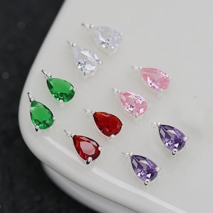 May include: A set of 10 teardrop-shaped crystal earrings in various colours, including clear, green, pink, red, and purple. The earrings are silver-toned and have a simple design.