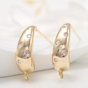 May include: A pair of gold hoop earrings with small clear rhinestones. The earrings are open and have a curved shape.
