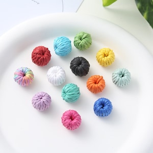 May include: Assortment of 12 colourful, woven, donut-shaped beads. The beads are made of a natural material and have a rustic, handmade look.