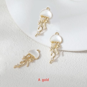 May include: Three gold-colored jellyfish charms with white tops and dangling tendrils. Each charm is adorned with small, clear crystals. The text "A gold" is visible at the bottom of the image.