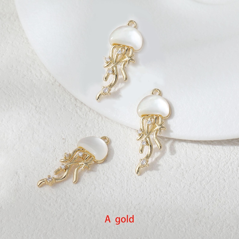 May include: Three gold-colored jellyfish charms with white tops and dangling tendrils. Each charm is adorned with small, clear crystals. The text "A gold" is visible at the bottom of the image.