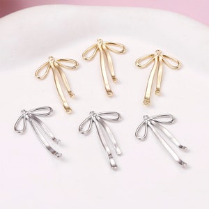 May include: Six gold and silver bow-shaped metal charms with a loop at the top. The charms are designed to be used for jewellery making or other craft projects.