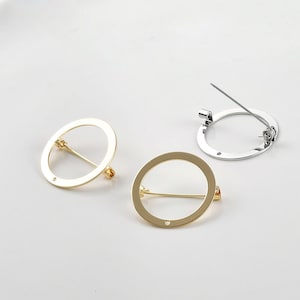 May include: Two gold and one silver circular brooch pins with a pin and catch closure. The brooches are simple and elegant.