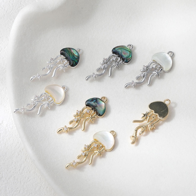 May include: A collection of jellyfish charms in silver and gold tones. The charms feature iridescent, white, and gold-colored tops with delicate, flowing tentacles. Some charms are adorned with small, sparkling accents.