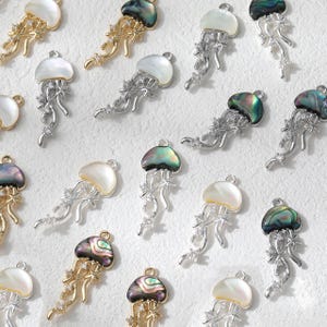 May include: A collection of jellyfish-shaped pendants. Some are gold-toned with abalone shells, others are silver-toned with mother-of-pearl shells. Each pendant features delicate tentacles and sparkling accents, perfect for jewelry making.