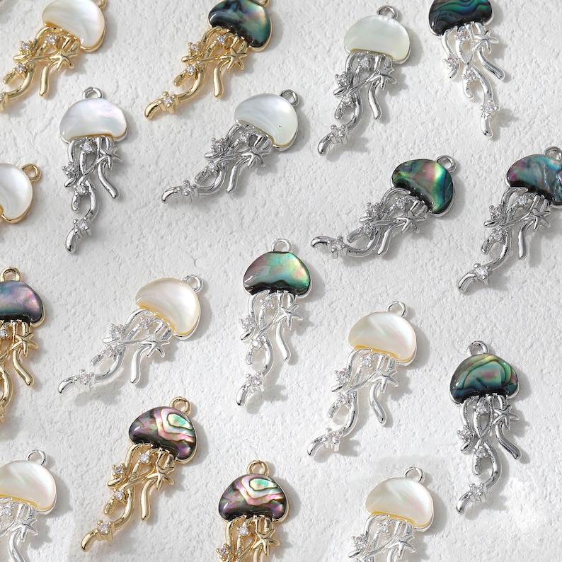 May include: A collection of jellyfish-shaped pendants. Some are gold-toned with abalone shells, others are silver-toned with mother-of-pearl shells. Each pendant features delicate tentacles and sparkling accents, perfect for jewelry making.