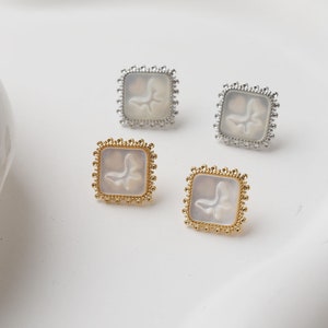 May include: A set of four square earrings with a delicate, ornate gold frame and a white, textured butterfly design inside. The earrings are available in gold and silver.