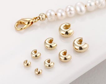 May include: A collection of gold-colored jewelry findings, including C-shaped crimp beads and a lobster clasp. A pearl necklace is also visible. The findings are arranged on a white surface, showcasing their metallic shine.