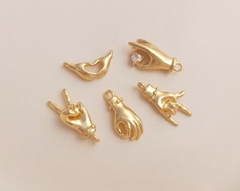 May include: Five gold-tone metal hand charms. The charms are in different hand gestures, including peace sign, heart, rock and roll, and a hand holding a small clear rhinestone.