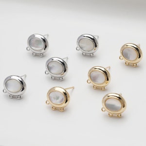 May include: Six oval-shaped earring findings with a white mother-of-pearl inlay. Three findings are gold-toned and three are silver-toned. Each finding has three small loops on the bottom for attaching a dangle.