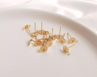 May include: A group of gold-toned earring posts with a loop on the back. The posts are scattered on a white surface.