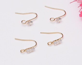 May include: Four gold earring hooks with clear crystal accents. Two hooks have round crystals and two hooks have rectangular crystals.