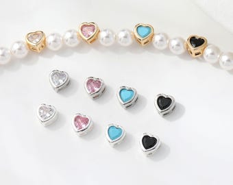 May include: A collection of heart-shaped charms in various colors, including clear, pink, turquoise, and black. Some charms are set in gold or silver-toned metal. A pearl necklace is also visible.