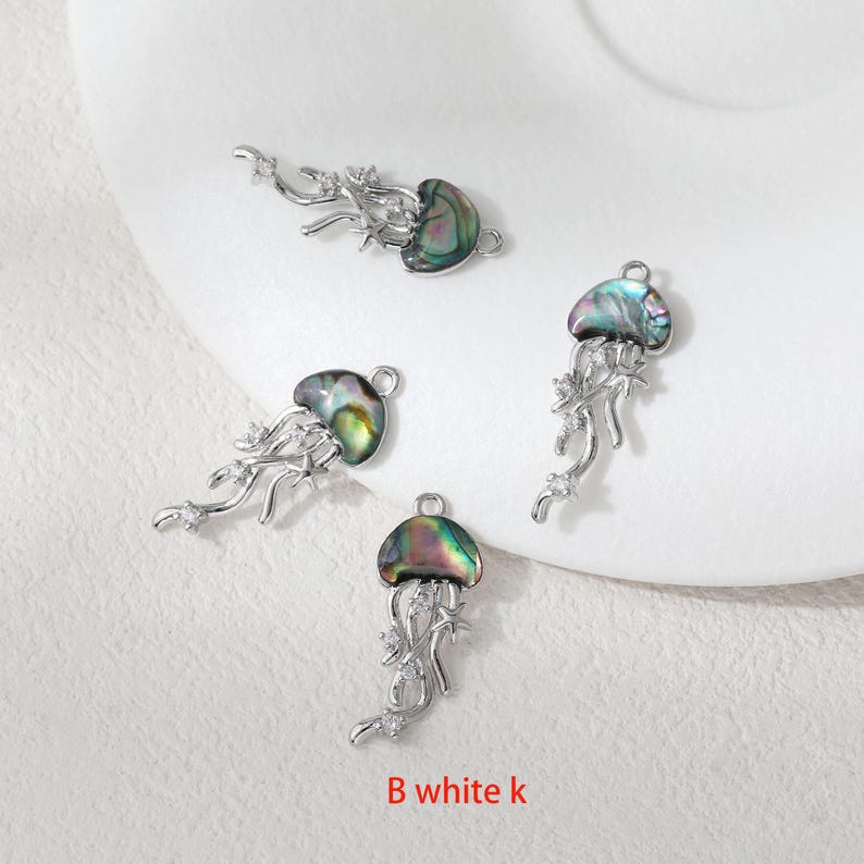 May include: Four silver-toned jellyfish charms with iridescent shells and delicate, flowing tentacles. Each charm features a loop for easy attachment and is adorned with small, sparkling accents. The text "B white k" is visible at the bottom.